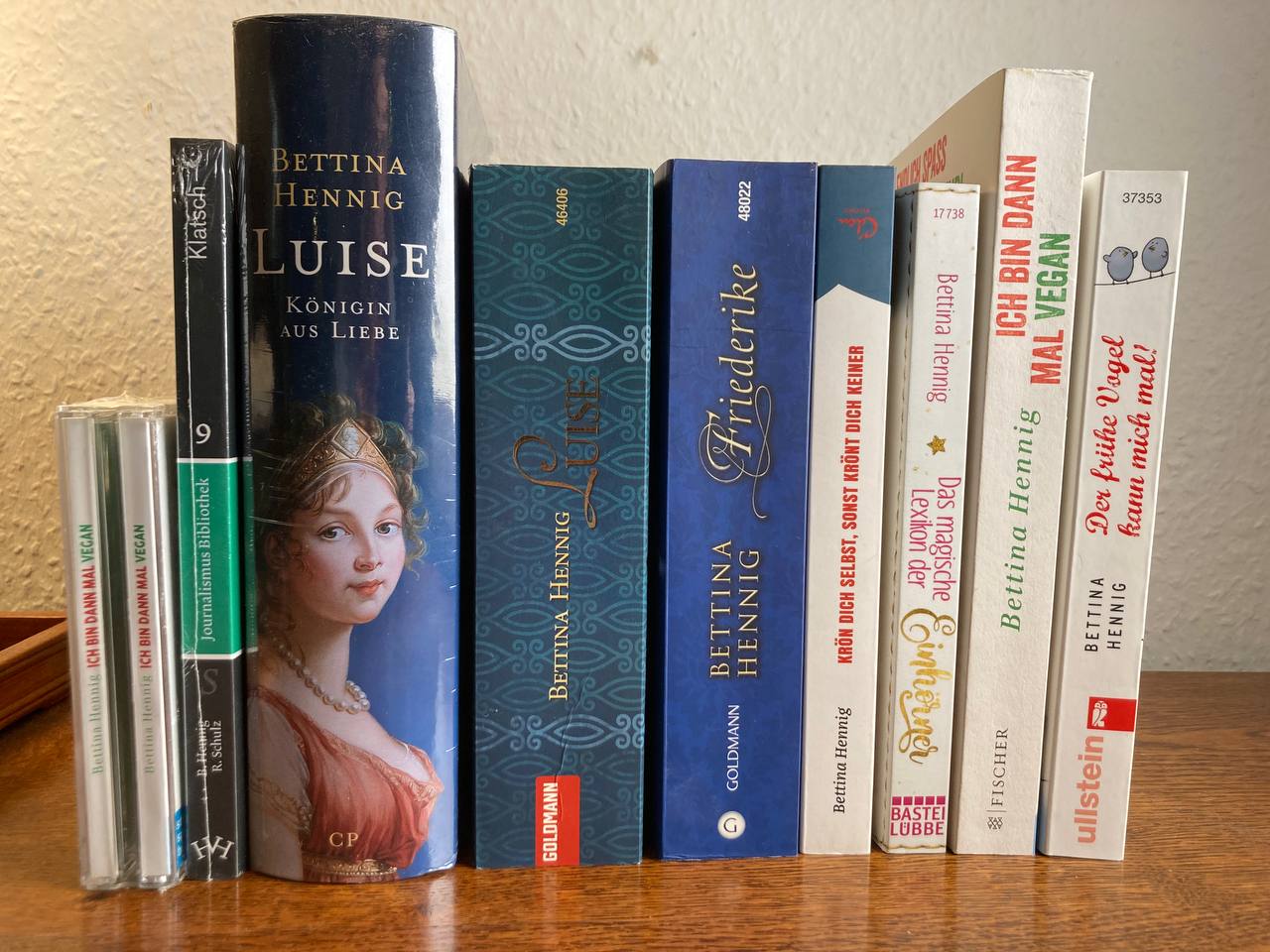 Das Bild zeigt neun Bücher und ein Hörbuch hochkant aufgestellt vor einer weißen Wand. Das sind die Bücher, die Bettina Hennig geschreiben hat.